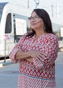 Diana Lerma Pfeifer wears a colorful shirt and stands next to a bus