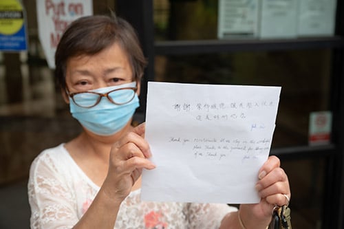 Asian woman holds up a sign written in her native language with an English translation below it