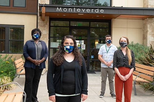 Eden Housing staff stand outside, wearing masks, in front of affordable homes called Monteverde