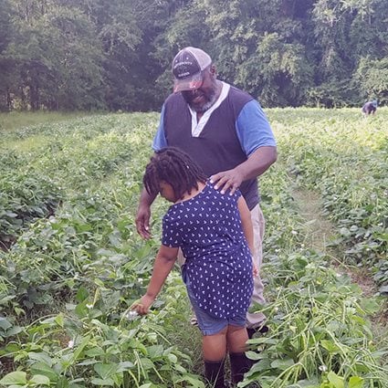 Ricky Dollison, a black farmer from Poulan, Georgia who raises pigs and grows row crops, stands in the field with his daughter