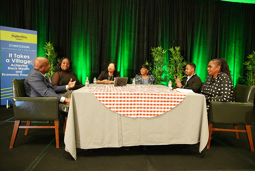 Black community and nonprofit leaders sit around a table styled like a kitchen table at NeighborWorks America's symposium "It Takes a Village: Achieving Black Wealth and Economic Prosperity"