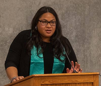 A young woman of color stands at a podium to give her graduation speech