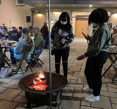 Two women hold their marshmallows over the fire to make s'mores.