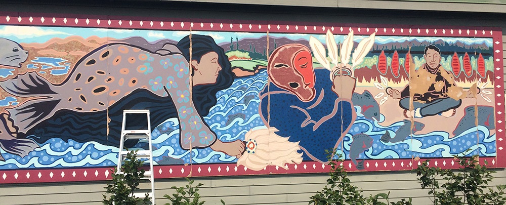 A mural shows a Native Alaska woman on the side of a building.