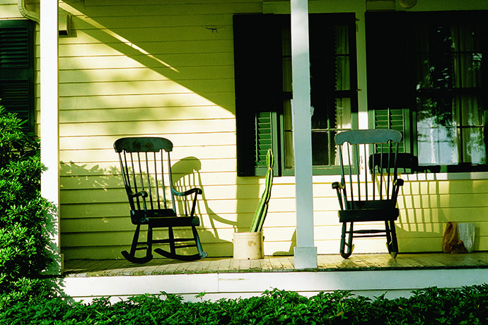 Photograph of a yellow-painted home with two rocking chairs on the porch