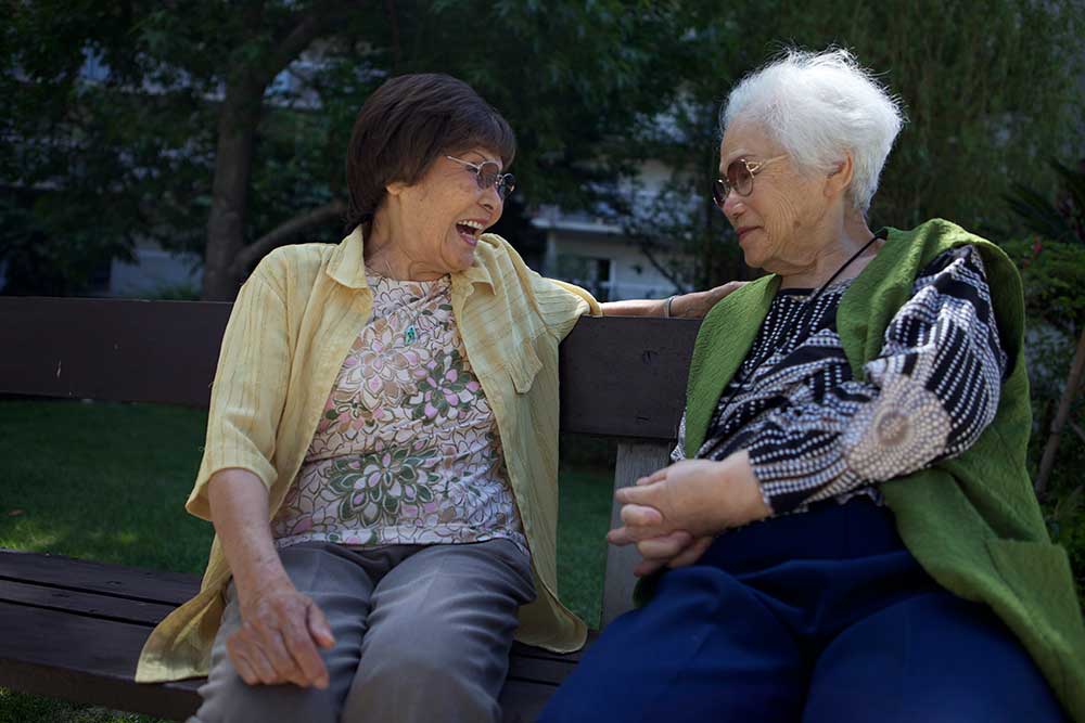 Two Asian women sit on a park bench outside