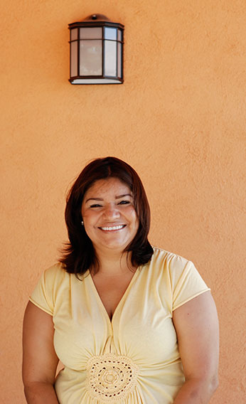 A Hispanic woman stands in front of her new home