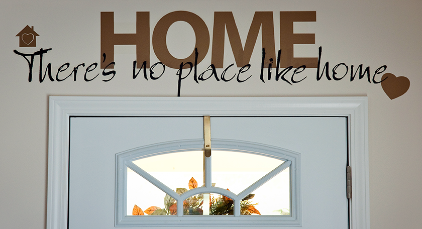 A sign above a white door that says: "Home. There's no place like home."