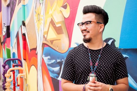 A VISTA member stands in front of a colorful mural