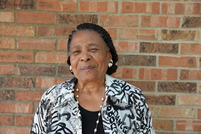 Gladys Muhammad stands against a brick wall.