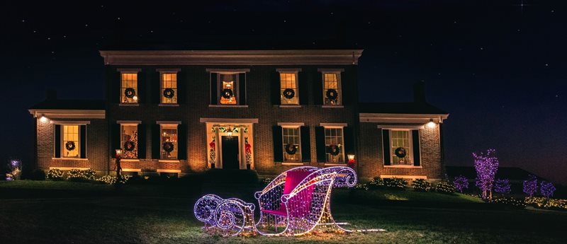 A house, with wreathes on the window, stands behind a glowing open sleigh.