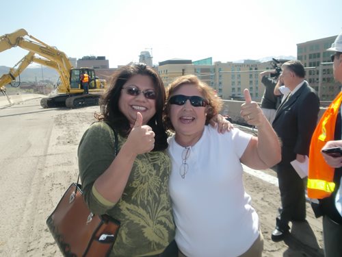 Maria Garciaz in front of a construction site, with yellow construction equipment behind her.