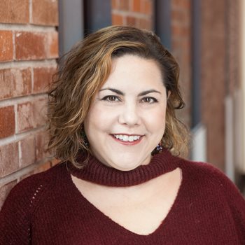 Sarah Chenven stands in front of a brick wall.