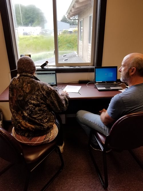 A man sits at a computer, receiving assistance from a volunteer, who helps him file a form so he can receive a stimulus payment.