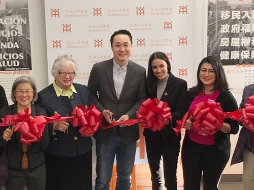 A ribbon cutting features Thomas Yu at the ready, with a pair of scissors. He is surrounded by coworkers and they hold a long red ribbon.