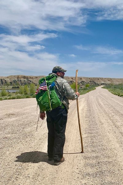 Tommy Zurhellen walks down an open road with a walking stick on his trek across the U.S.