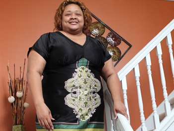 A black woman wearing a black dress stands in her newly-renovated home