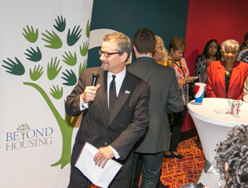 Beyond Housing's executive director stands next to the organizations banner at a community meeting