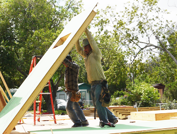 Two men lift the side panel of a new home