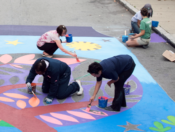 A mixed group of people paint a sidewalk