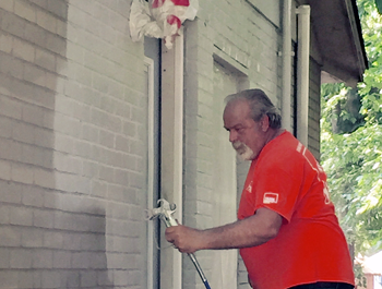 A man wearing an orange shirt power washes the side of a home