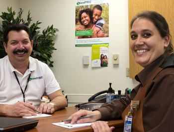 A man holding a pen and a woman signing documents smile at the camera