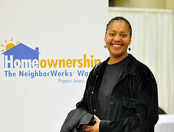 A black woman stands next to a LIFT homeownership banner