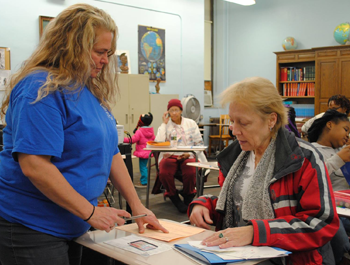 A white woman wearing a blue shirt goes over tax information with an older white woman in a red, gray and white jacket