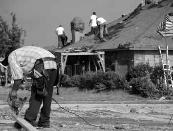 A group of people standing on top of a roof working on a house.