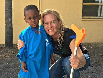 A black boy wearing a blue shirt stands next to a white woman