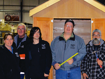 A mixed group of people stand in front of a shed