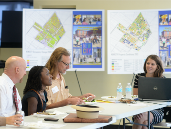 A group of four people sitting at a table in a classroom environment, talking.