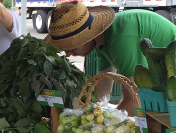 A white man wearing a green shirt and straw hat looks at vegetables at the Sankofa Market in Rhode Island