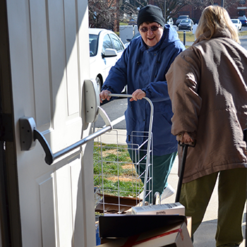 A woman wearing a blue hoodie delivers food to a senior