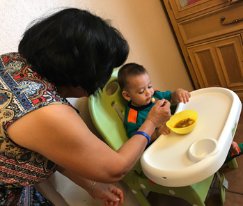 A woman feeds a baby sitting in a high chair