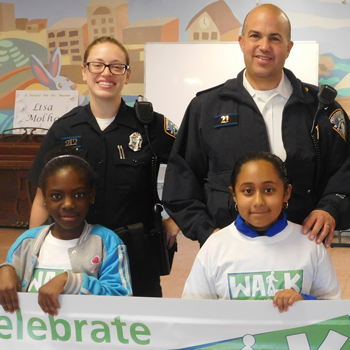 Office Tracie Miller and Lt. Richard Fernandes stand behind Olneyville youth holding up a "celebrate" sign