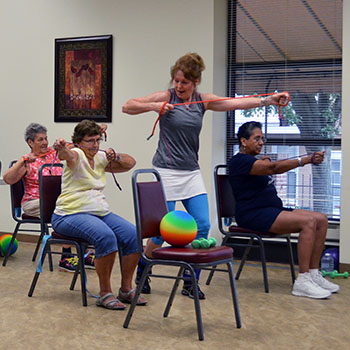 A white woman demonstrates to three seniors how to stretch