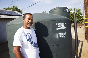 Self-Help Enterprises employee stands in front of a black water tank